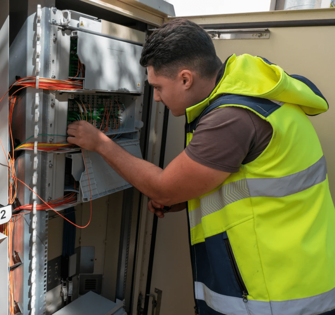 Technician servicing fiber optic telecom cabinet outdoors